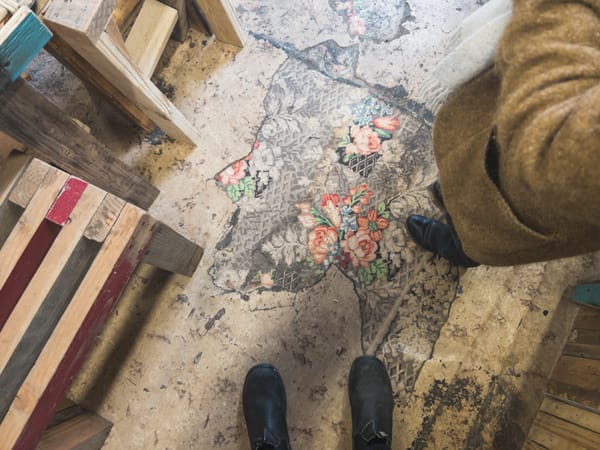 POV view of concrete woodworking shop floor, scabs of old gray tile with pink flower ornaments.