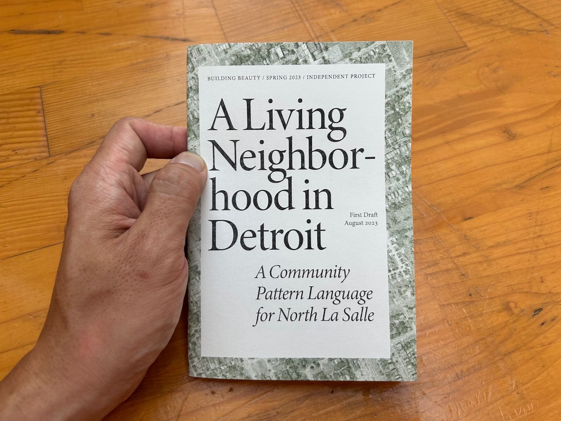 Hand holding cover of zine, titled “A Living Neighborhood in Detroit”