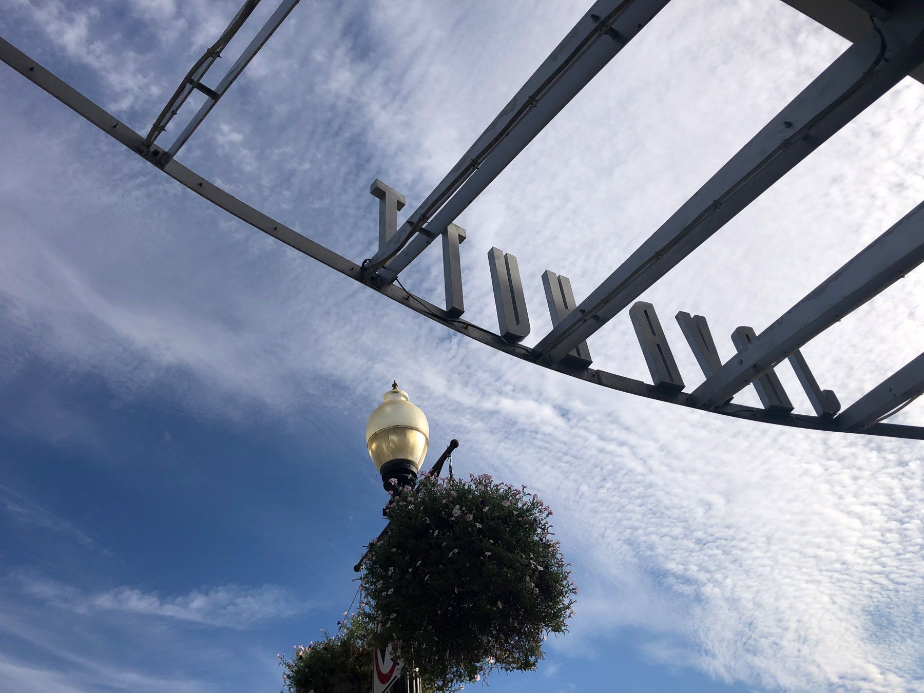 Cutout metal sign from reverse; blue sky and thin clouds in the background.