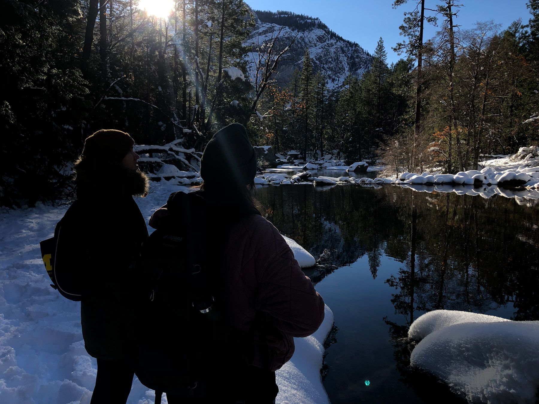 Standing by still, snowy lake. Sun coming through tree branches.