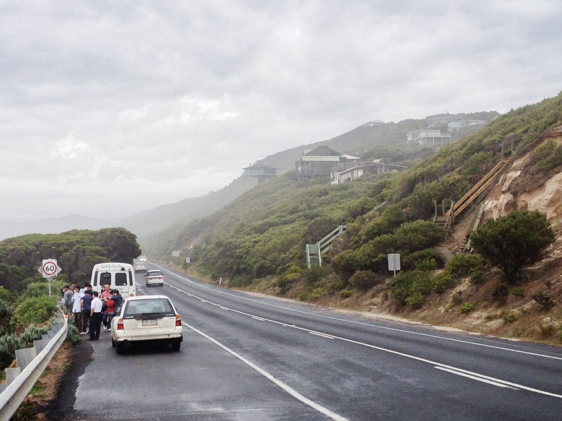 Passengers pulled over along the side of the road, opposite foggy greenhills.