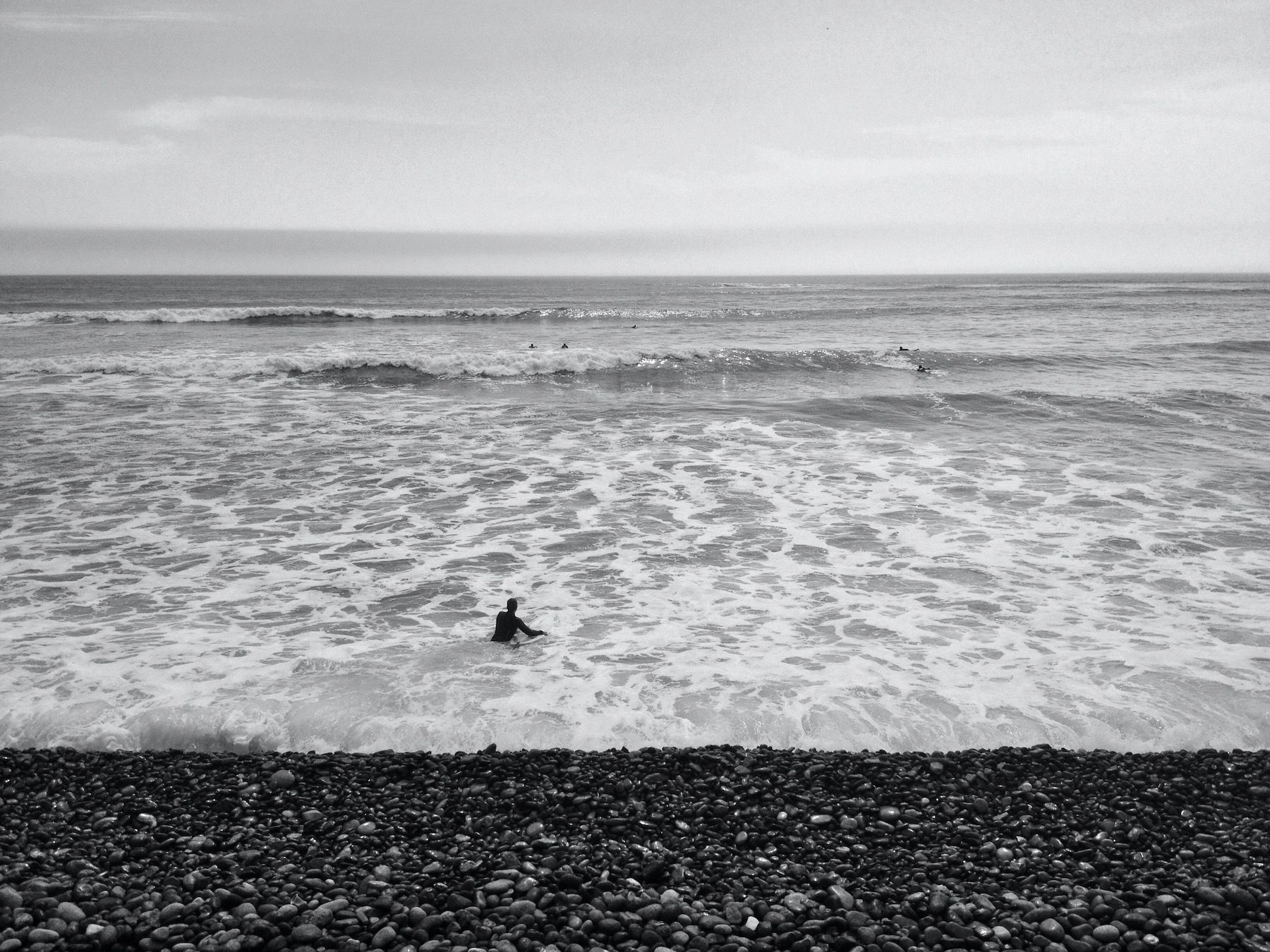 Black and white, surfers and rocky beach.