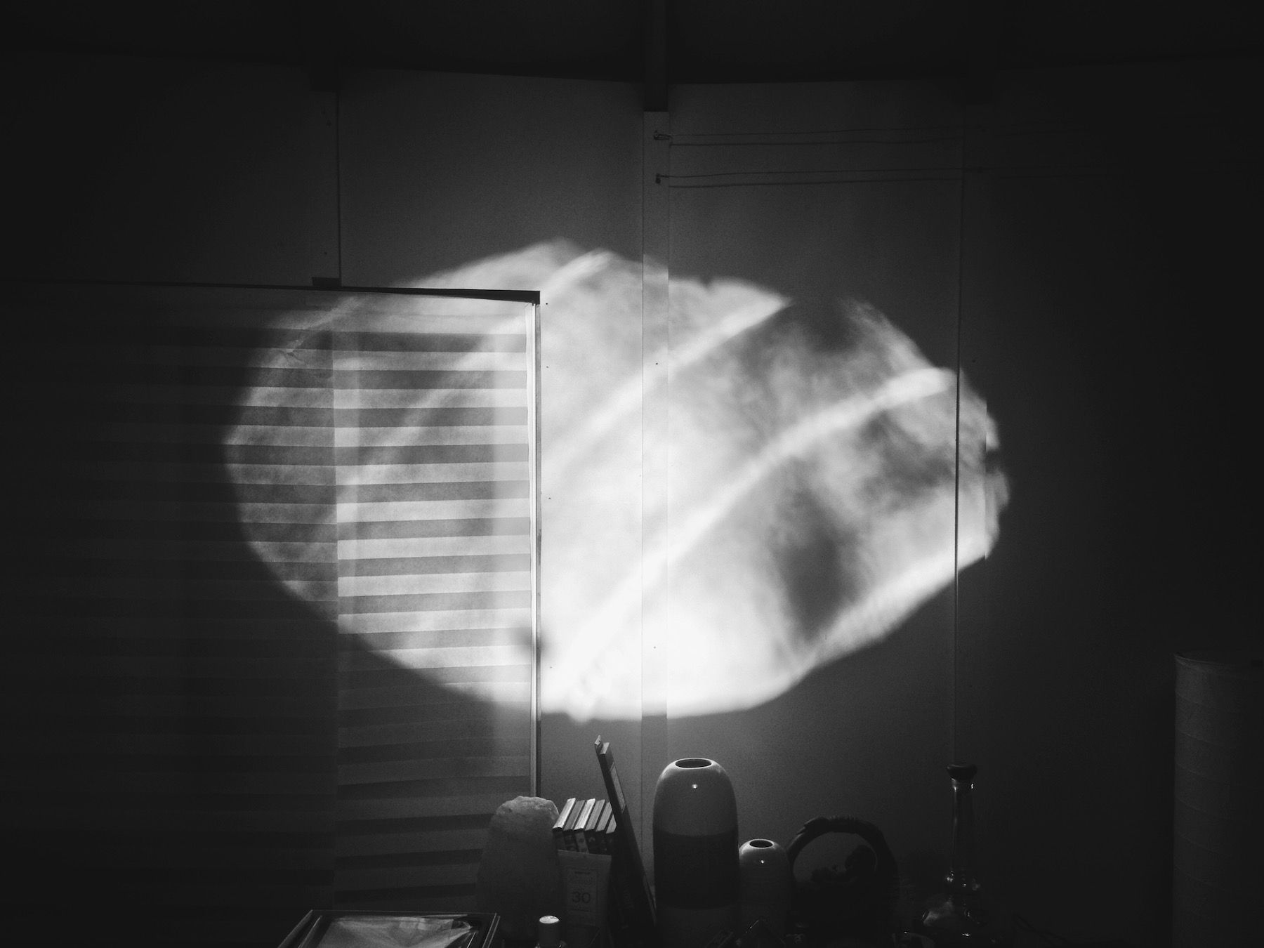 Black and white. Oval oculus-light in shadowy yurt, outlines of vases and closed blinds.