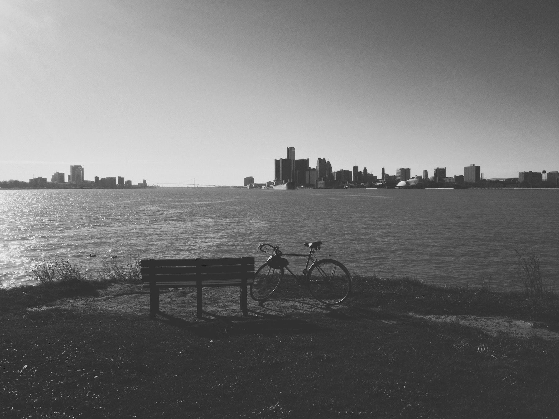 Black and white bike parked next to bench. Detroit river and skyline in background.