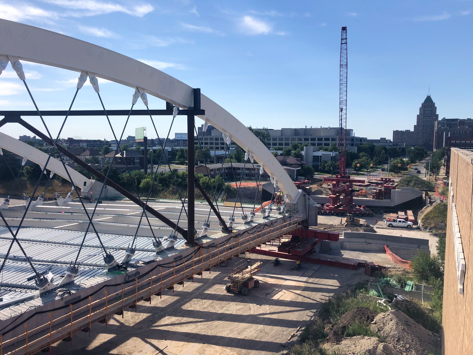 Tied Arch Bridge getting ready to be moved over I-94. Red cranes and tracks, Fisher Building in background.