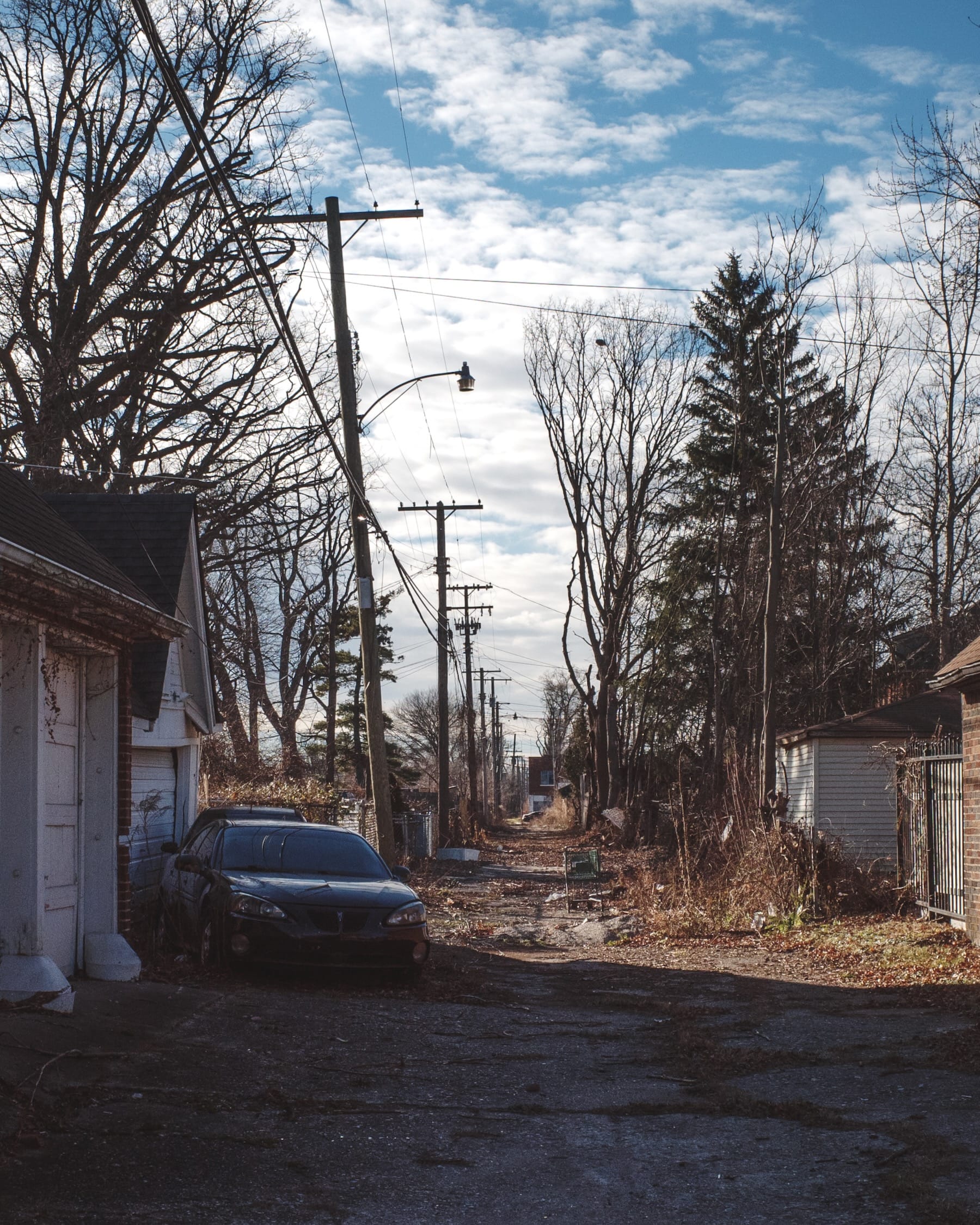 Dry winter alley with cracked pavement, power lines, old car and empty shopping cart.