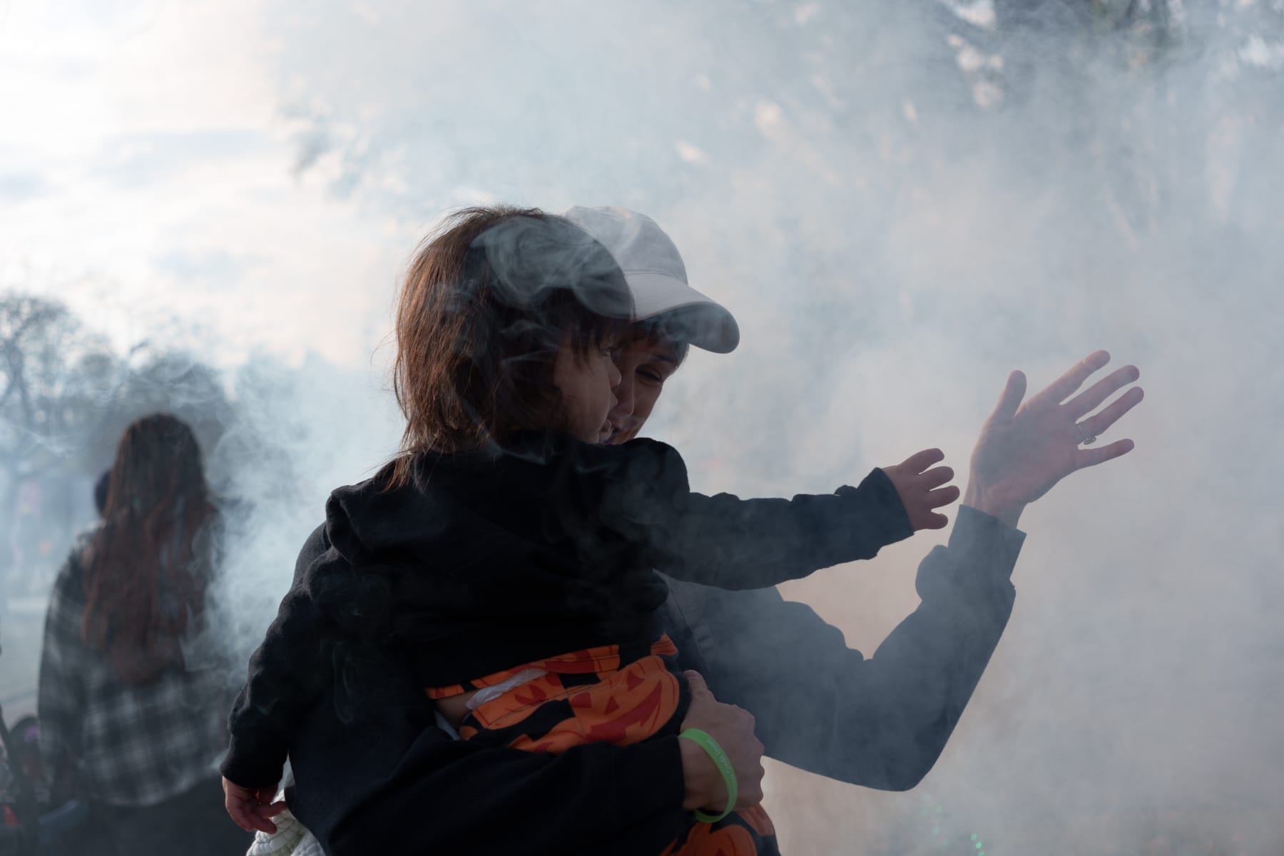 Julia carrying Rufus, wearing a pumpkin outfit, playing with smoke at an outdoor Halloween event at the zoo.