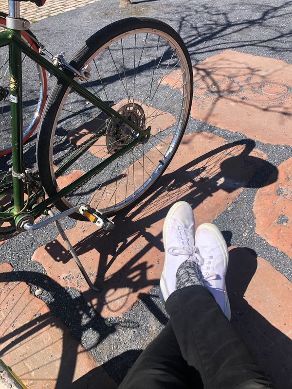 Parked bikes in the sun; pea gravel pocked with large stones from old buildings; my white-sneakered feet.