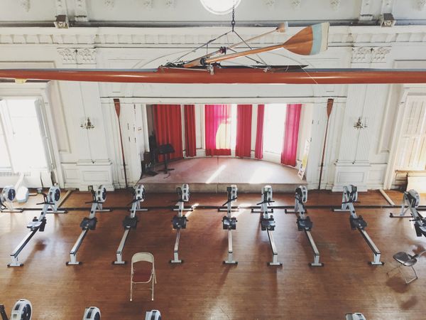 Rowing machines in a row, audienced toward a semicircular stage. Wood floors. No people.