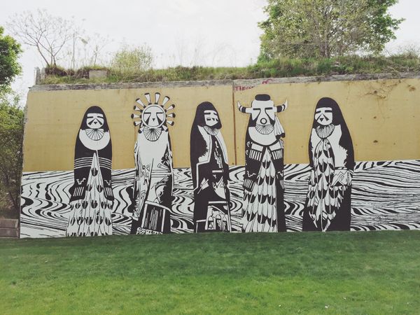 Street art along walls of greenway; black and white masked tribal figures over white background.