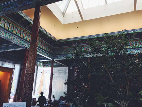 Carved wood trim and columns, painted teal, yellow and red; small tree reaching up toward interior skylight.