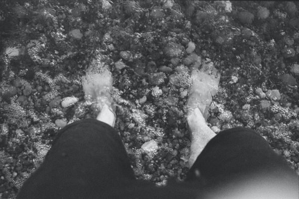 Black and white. Feet in pebbly water, incoming tide.