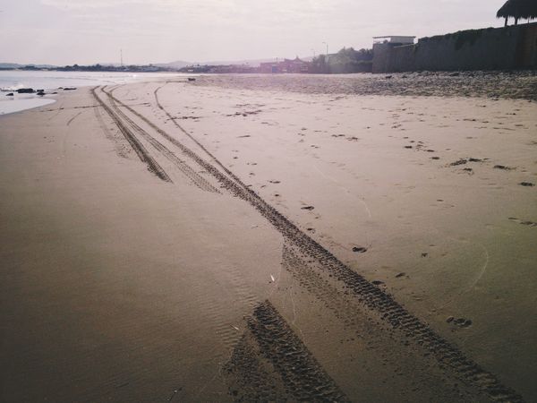 Wave-swept tire tracks on a beach.
