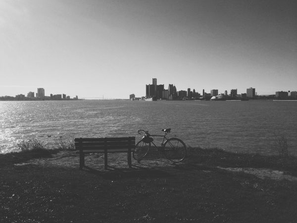 Black and white bike parked next to bench. Detroit river and skyline in background.