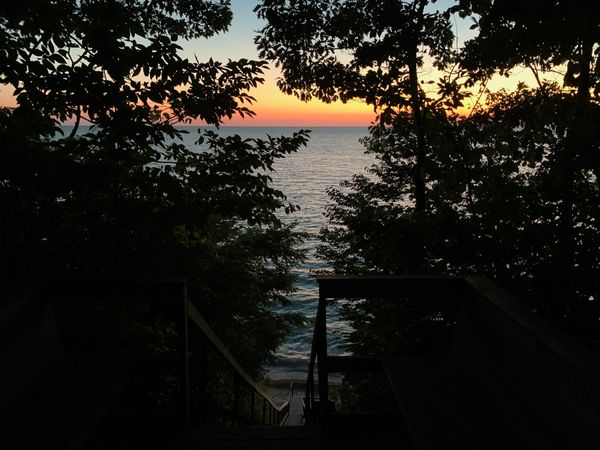 Wooden staircase down to Lake Michigan sunset, through silhouette of trees.