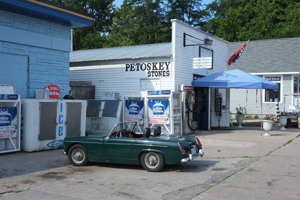 Teal vintage convertible parked in front of white clapboard shop with tin roof, and sign reading Petoskey Stones.