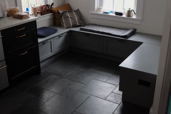 Bluish-gray breakfast nook in cloudy morning light. Black pulls, black slate floor. Pillows and blankets.