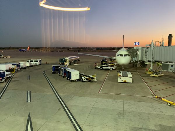 Purple and orange sunset over airport runways. Plane parked at gate. Airport reflection in glass.