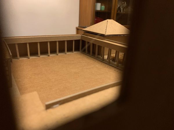 View through cutout window of a cloistered cardboard courtyard.